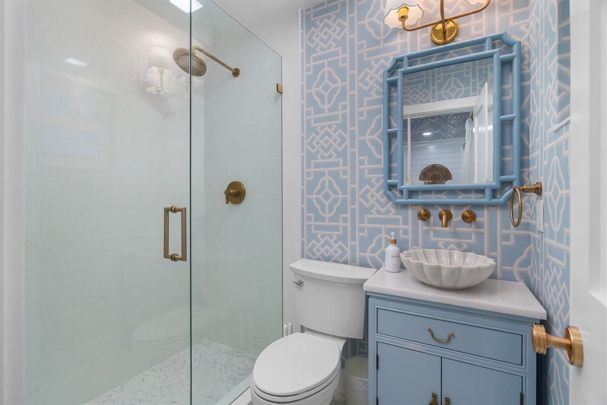 A designer bathroom featuring custom blue cabinetry, a statement bowl sink, and warm metallic accents set against bold geometric tile.
