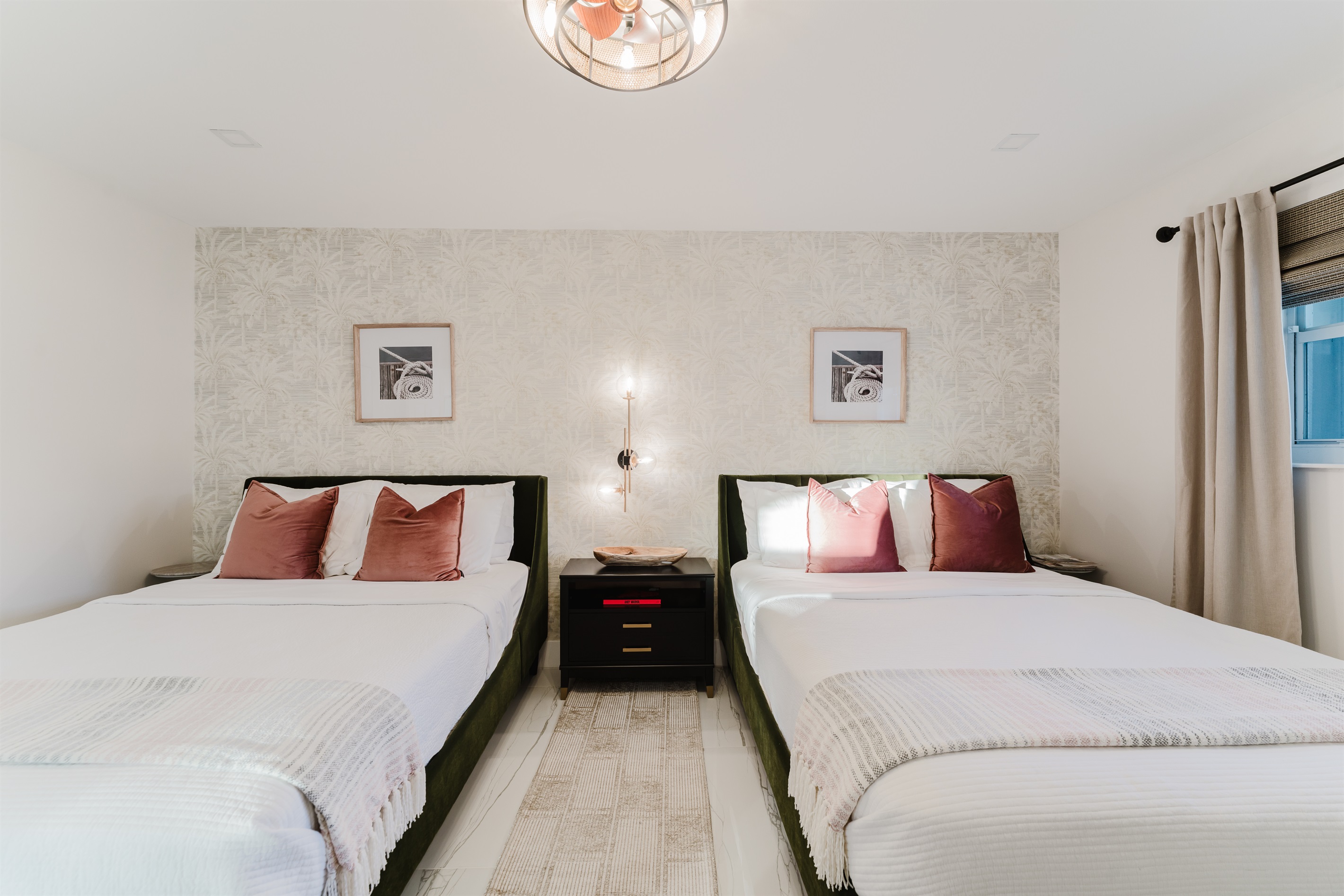 Bright coastal suite with two queen beds, private ensuite bath, smart TV, blackout bamboo shades, and a rattan ceiling fan—ideal for families or shared stays.