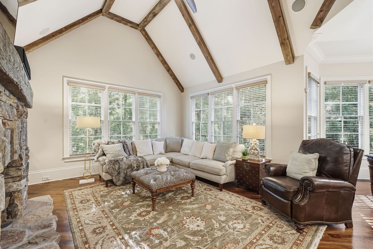 Relax in a warm and welcoming living room featuring high ceilings, a beautiful stone fireplace, and rich wood accents that create a cozy, home-like atmosphere. Enjoy a smart TV with a quality sound system perfect for movie nights and quiet mornings.