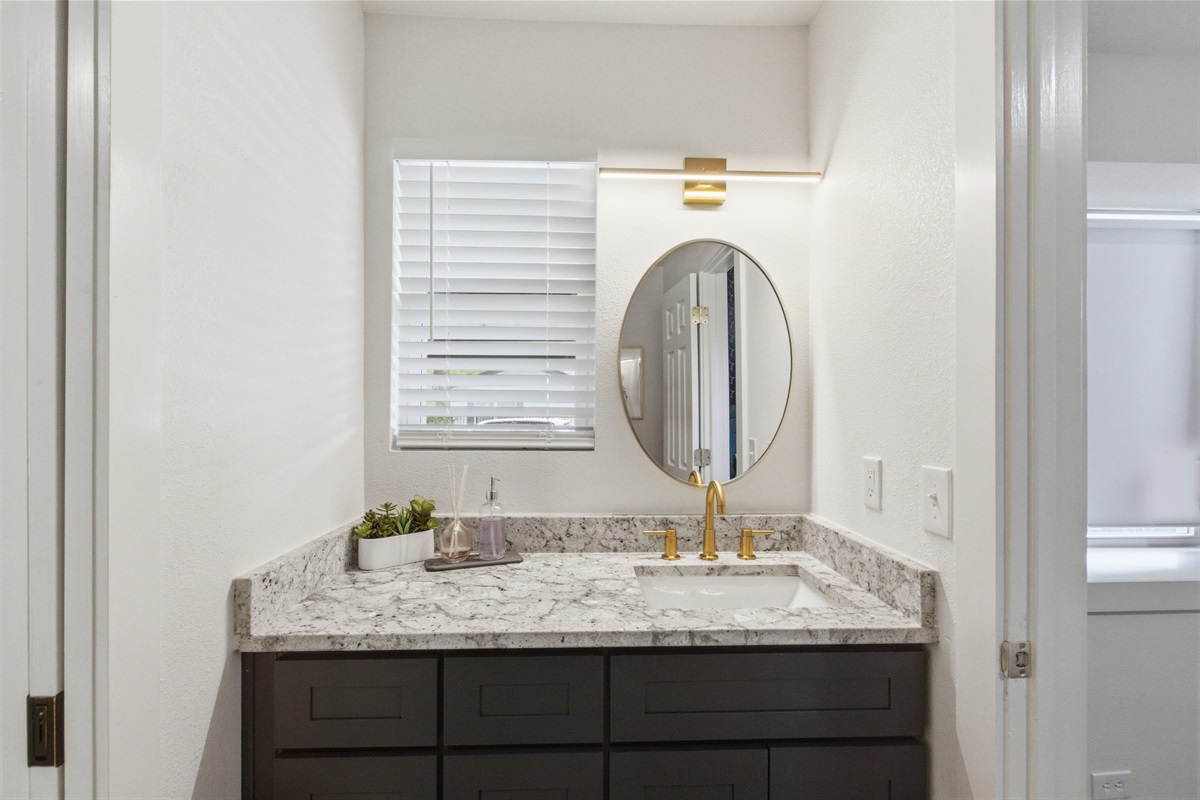 Dual vanity with round mirror, gold fixtures, and marble countertop. Stocked with Ginger Lily Farms bath essentials. One of 2.5 bathrooms in this 4-bedroom Arlington vacation rental.