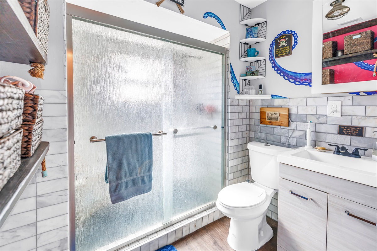 Clean bathroom with a walk-in shower, modern vanity, white tile accents, and colorful decor for a bright, welcoming feel.