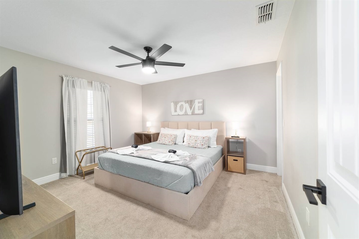 This inviting king bedroom offers a soft, calming design with plush bedding, warm lighting, and cozy décor. Relax in a spacious, comfortable setting featuring a large Smart TV and plenty of natural light— perfect for unwinding after a day of fun.