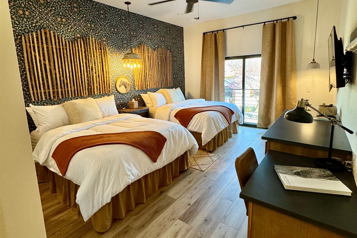 Corral Suite at Gaines Ranch on the Square — double queen beds in premium Comphy linens against a custom modern Western feature wall. Small desk, storage and sitting area for comfortable stay.

