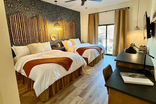 Corral Suite at Gaines Ranch on the Square &mdash; double queen beds in premium Comphy linens against a custom modern Western feature wall. Small desk, storage and sitting area for comfortable stay.