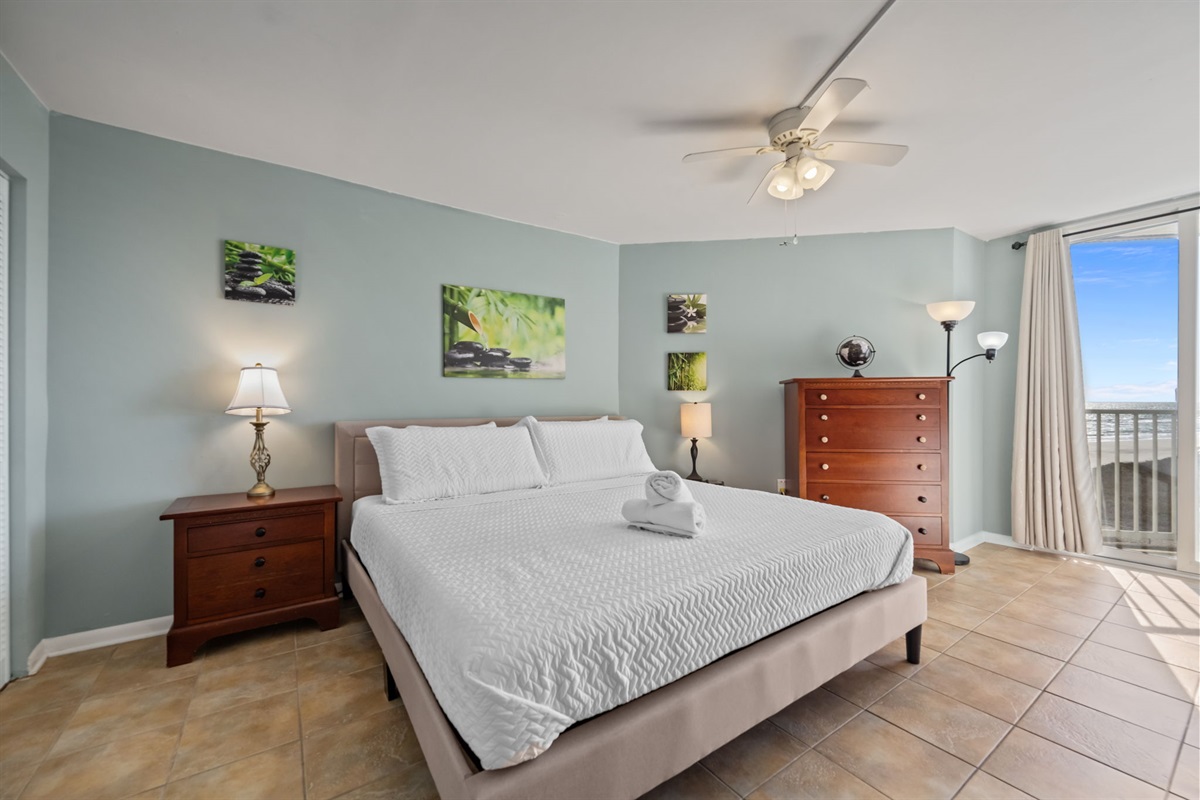Spacious Master bedroom with a comfortable King-size bed, dresser storage, ceiling fan, and sliding doors opening to oceanfront balcony!