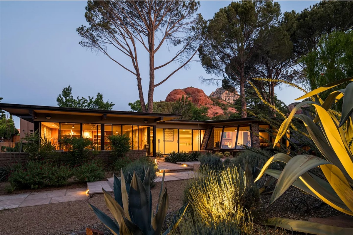 Striking mid-century modern home glowing at sunset, framed by desert landscaping and stunning red rock views in the background.