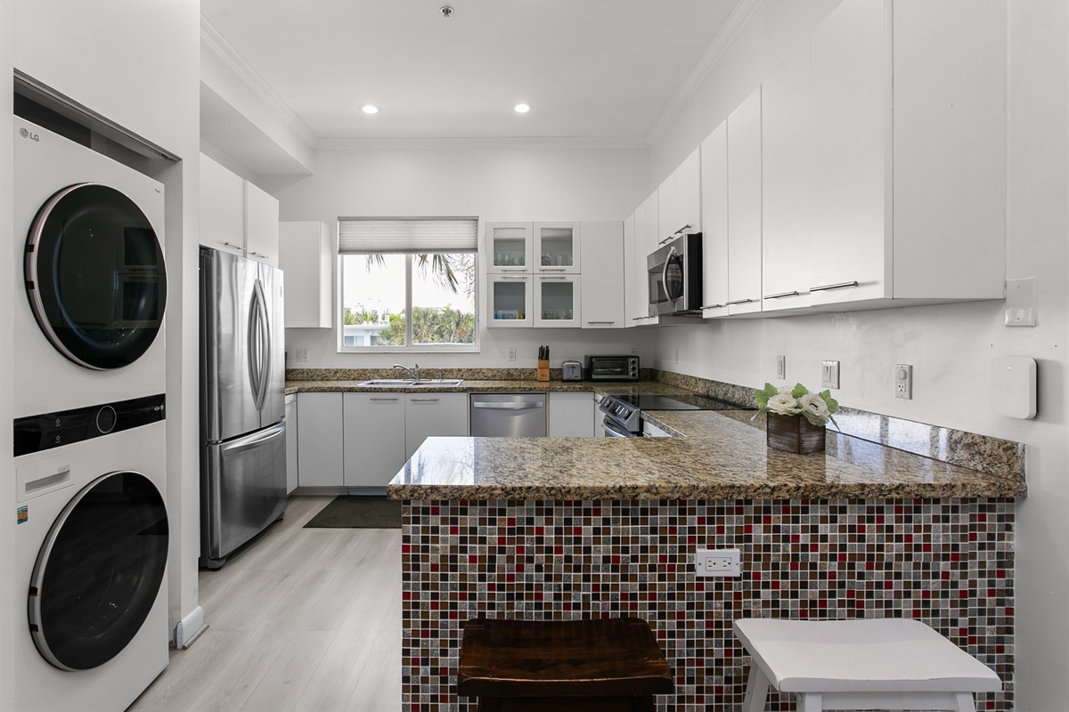 Induction range, French door fridge with bottom freezer, and breakfast counter. LG laundry tower right next to it.