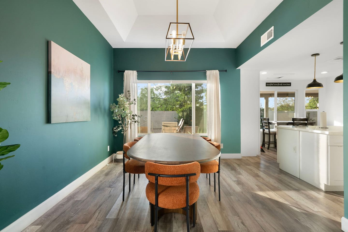 Sophisticated dining room with teal accent walls, round table, and views of backyard oasis. 
