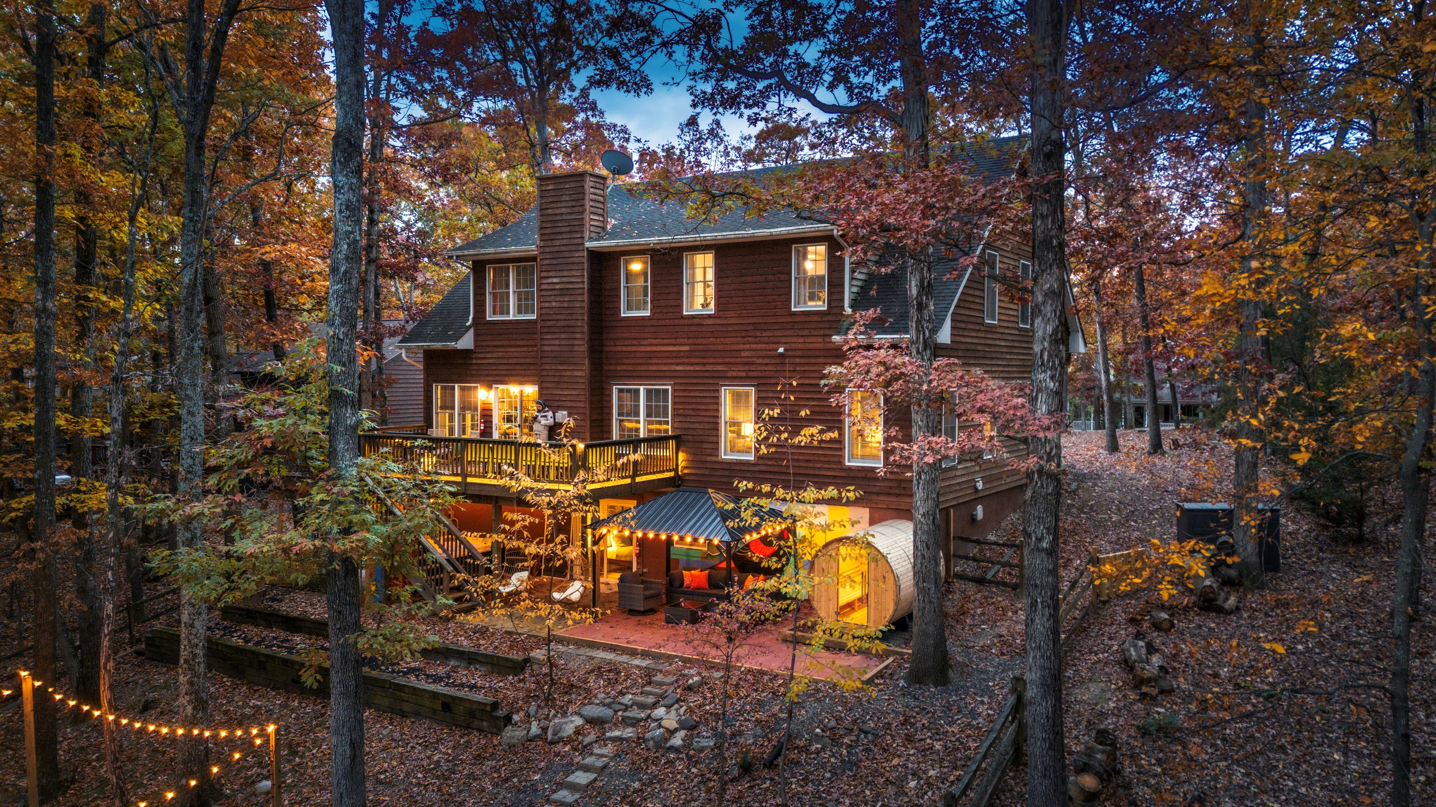 A true multi-level retreat — two living rooms, hot tub, sauna, game room + cozy hangout zones lit up under the trees.