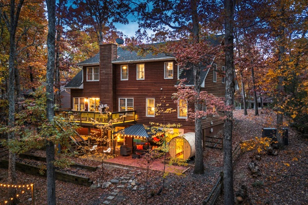 A true multi-level retreat — two living rooms, hot tub, sauna, game room + cozy hangout zones lit up under the trees.