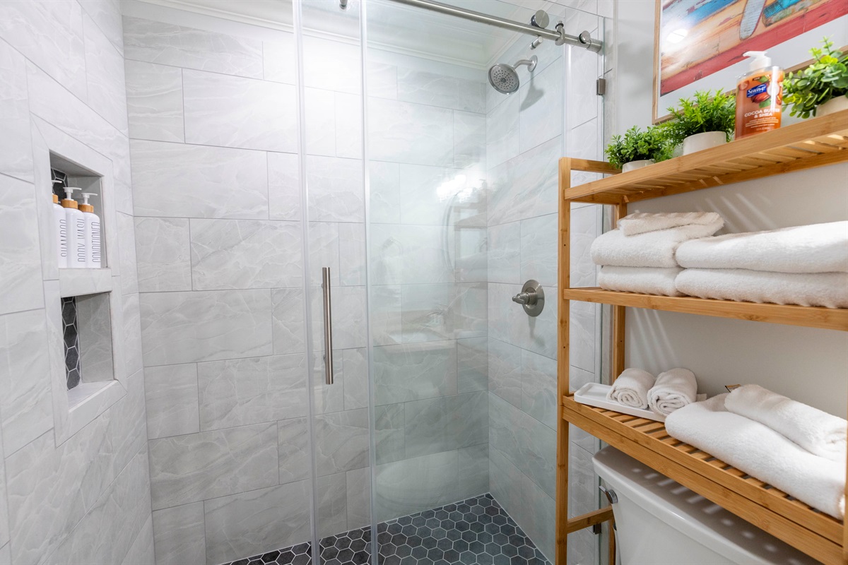 Modern bathroom with glass shower, wooden shelves, and fresh, cozy vibes!