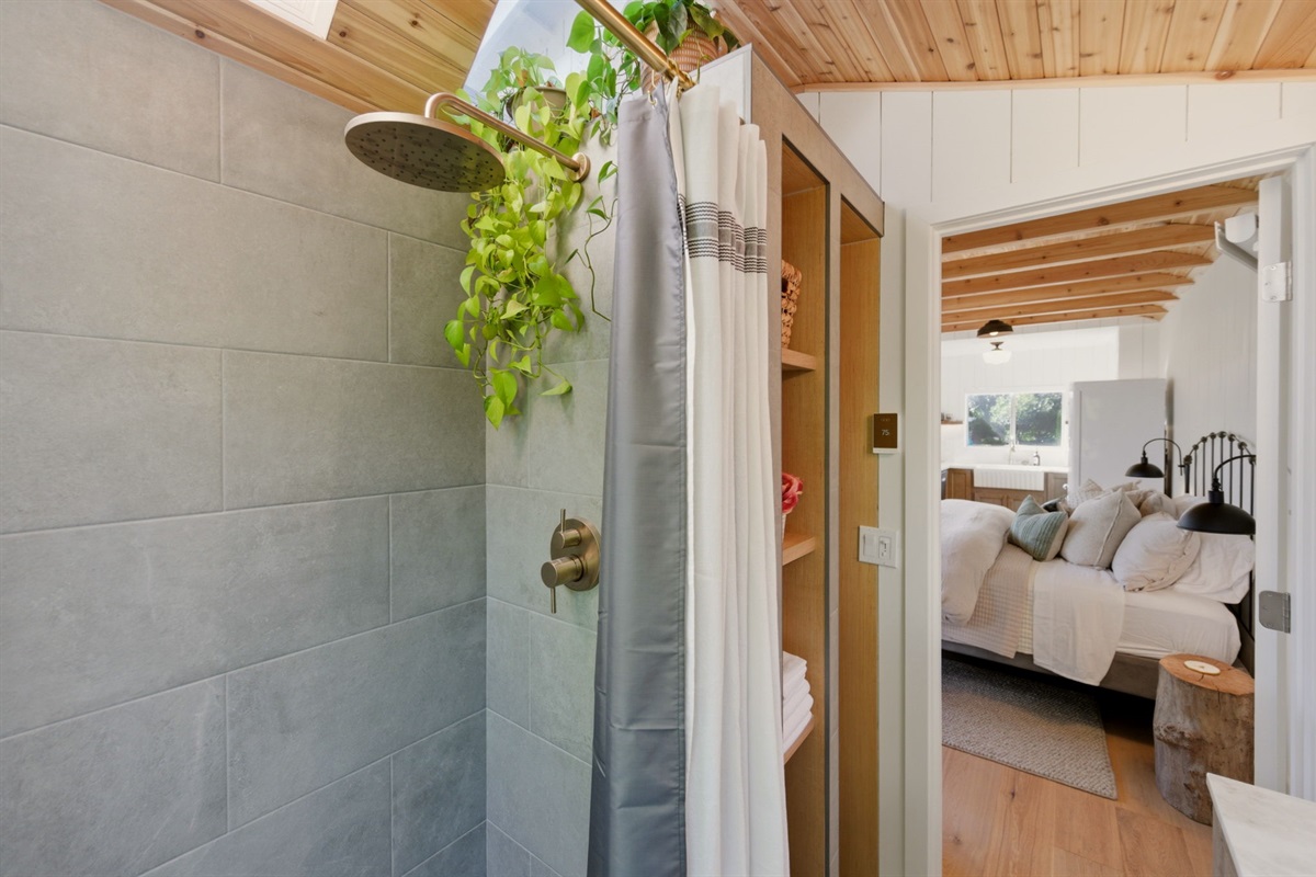 Unexpectedly luxurious for a tiny cottage, this serene spa bath offers heated floors, cedar warmth, a rainfall shower, and expansive lake views—while skylights overhead create the dreamy feeling of showering in the open air.