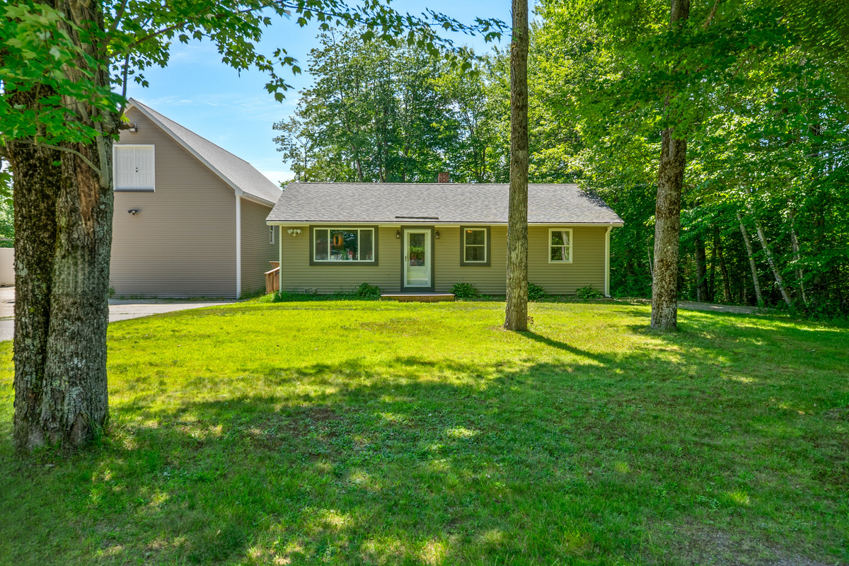 Walk across the front grass lawn shaded by mature trees to reach the main entry door. This ranch-style home layout keeps all core living areas on a single level, surrounded by a peaceful wooded yard setting in a convenient Lamoine location.