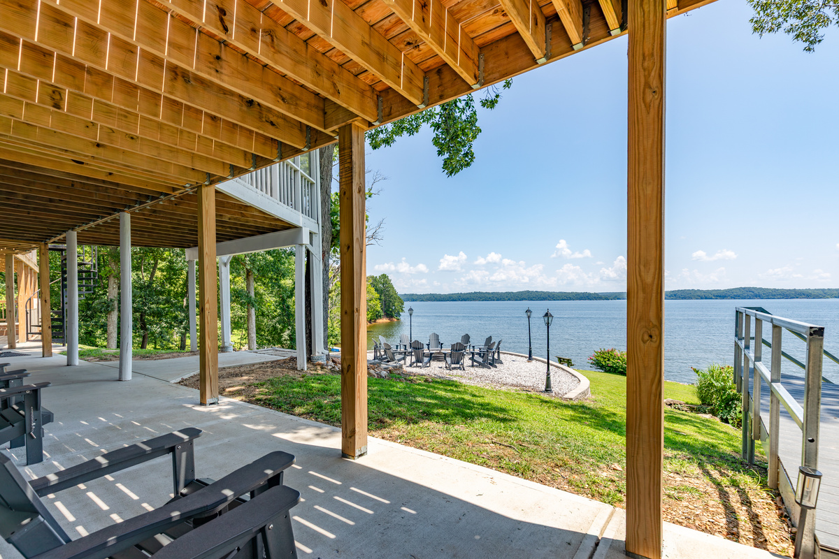 The covered lower patio keeps guests close to the lawn, firepit, private dock, and shoreline.