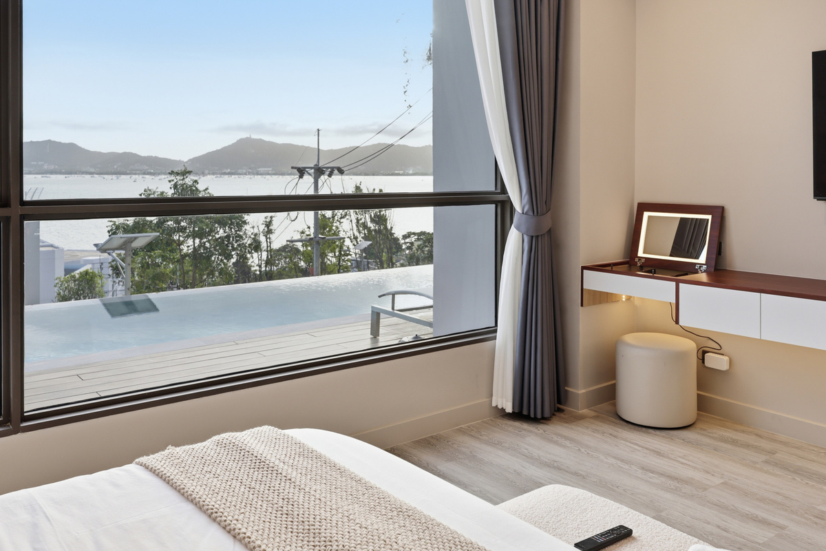 Bedroom with water and mountain views through floor-to-ceiling windows, vanity desk, and private balcony with seating.