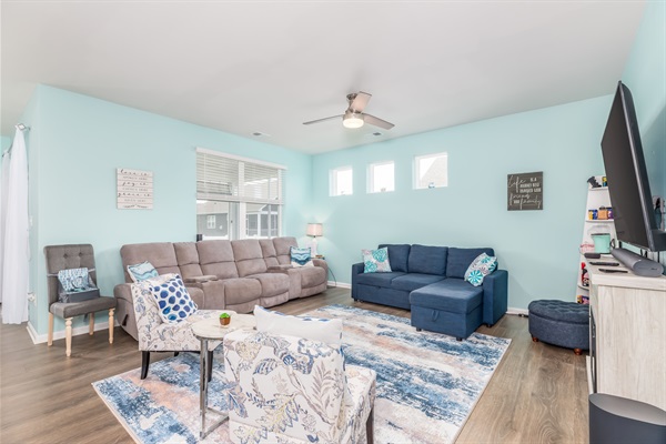 Bright family lounge featuring plush recliners, a versatile blue sleeper sofa, and a large smart TV—perfect for movie nights, game marathons, or just unwinding after a day of coastal fun.