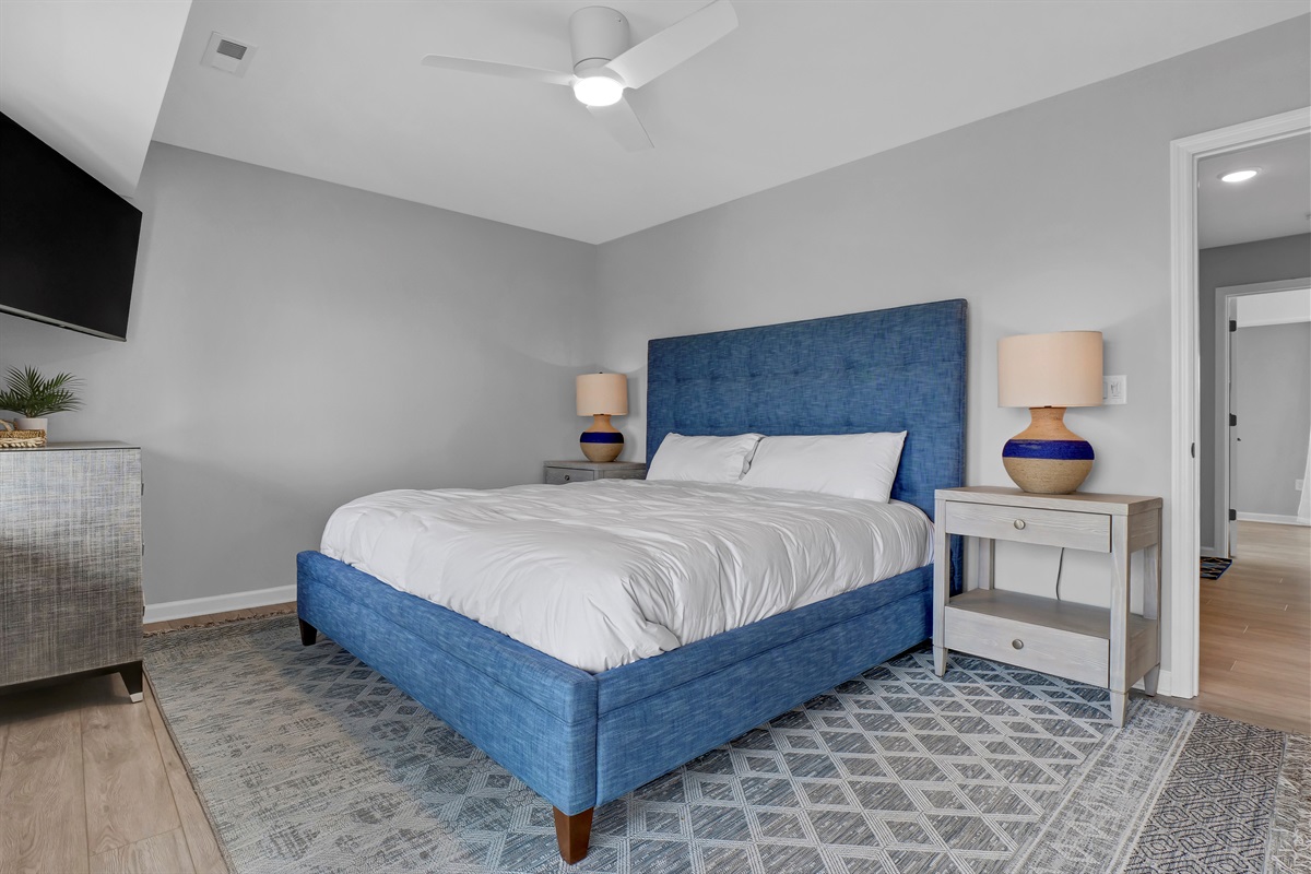 This primary suite features a plush king sized bed, smart TV, private balcony, plenty of storage, and an en-suite bathroom. 