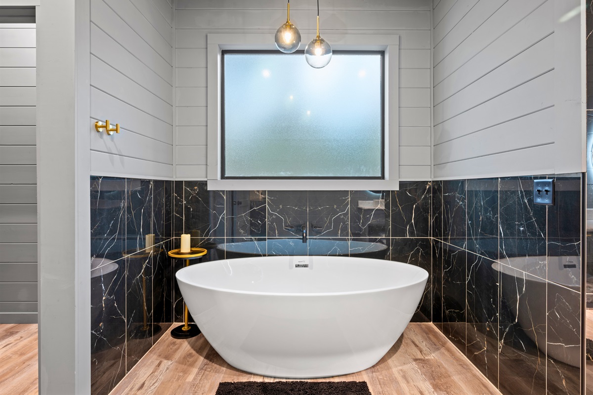 Positioned beneath a large window, the soaking tub offers a quiet spot to relax while enjoying views of the surrounding trees.