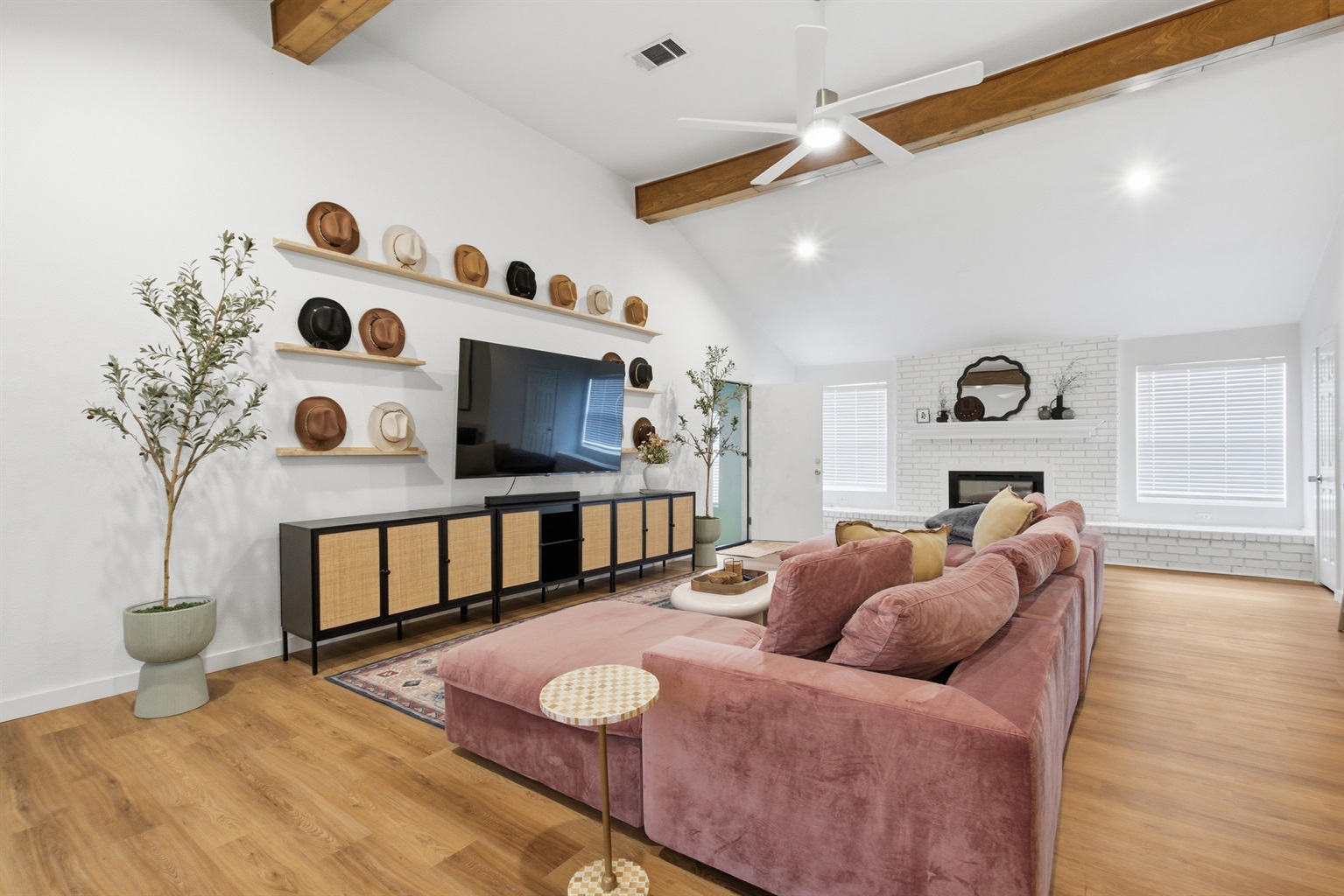 Main living room with 75" Smart TV, exposed wood beam ceiling, and sectional seating for 8. Hardwood floors and ceiling fan throughout.