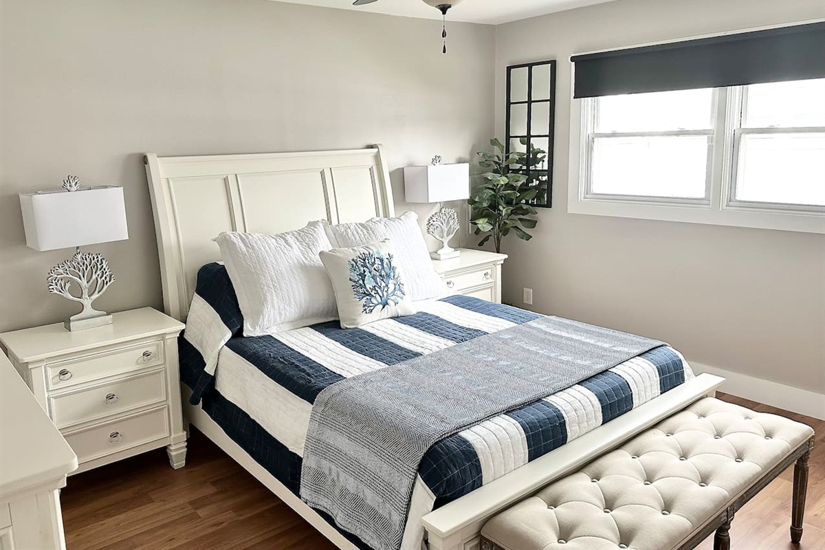 Rest easy in this bright bedroom featuring a white panel bed and matching nightstands. The space is accented by a tufted bench and coral-themed lamps, creating a serene, coastal atmosphere for a perfect night's sleep.