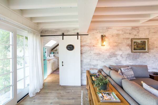 The barn door dividing the kitchen and living room was reclaimed from a Montecito teardown, the brick wall wears a hand-finished German schmear, and the bookshelf began life as an RH armoire that didn’t quite survive the move.