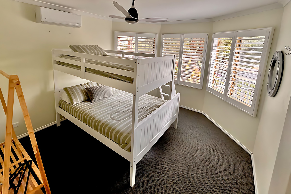 Bedroom 2 has a white tri-bunk with a double bed below and a single bunk above, plus plantation shutters, a ceiling fan and split-system air conditioning, on the same level as the living areas.
