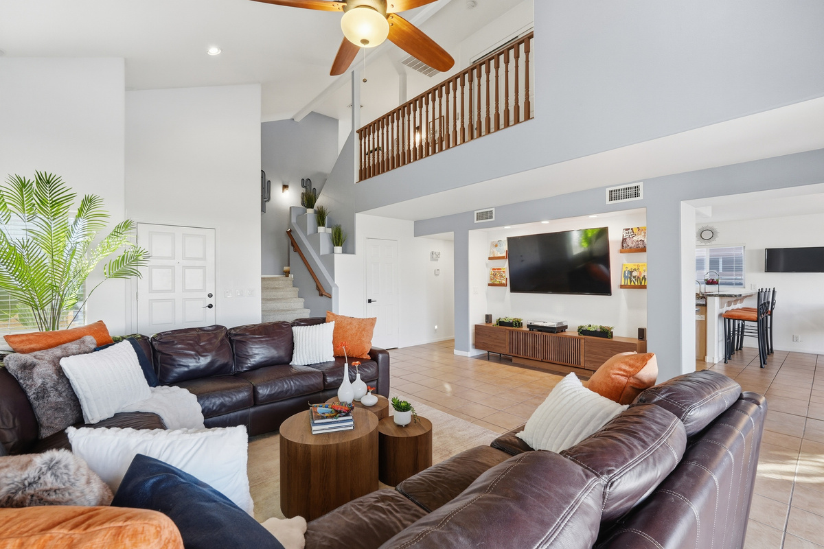 Living room with vaulted ceilings, leather sectional seating, large TV, and open flow toward the kitchen and dining area.