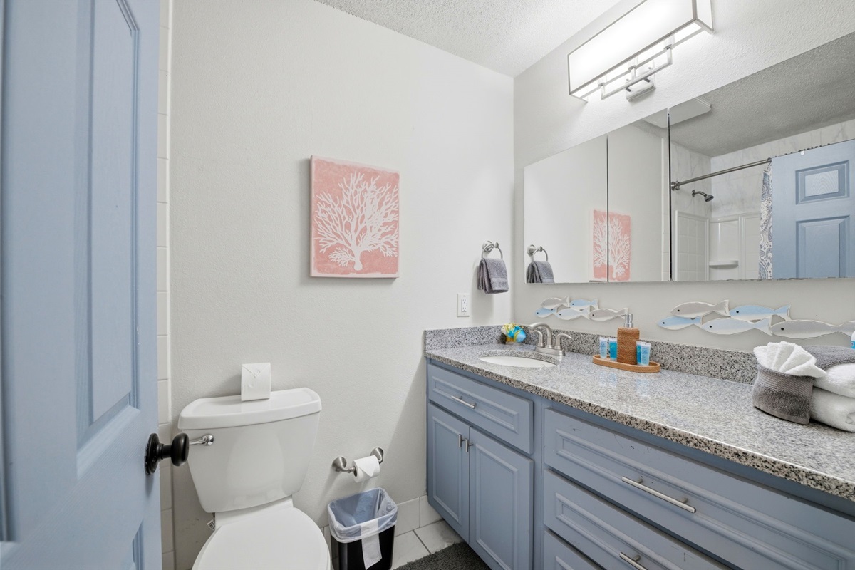 The bathroom offers a large mirror, granite vanity, and plenty of counter space for added convenience. With fresh towels and a shower-tub combo, it provides everything needed for a comfortable stay.