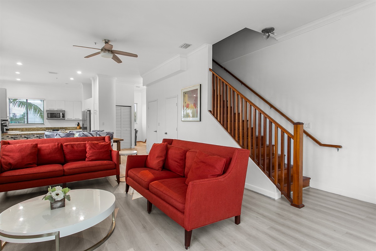 Huge sunny corner living room with two sofas, a daybed, and a swing chair. Private balcony with city and waterway views.
