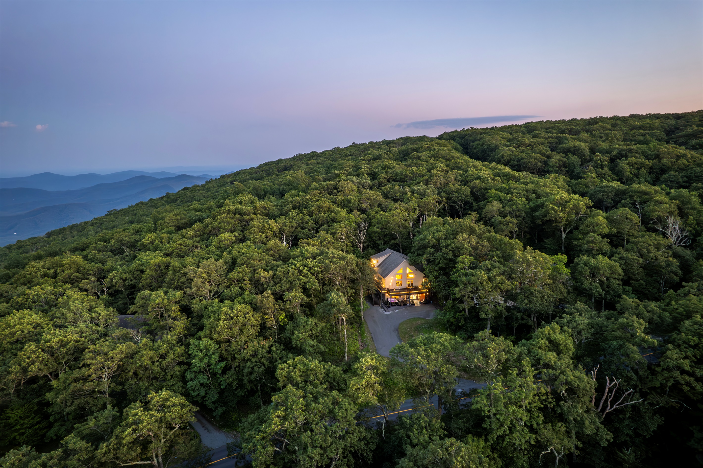 This mountaintop retreat glows golden at dusk, nestled among trees with endless layers of Blue Ridge views—a perfect balance of seclusion and access