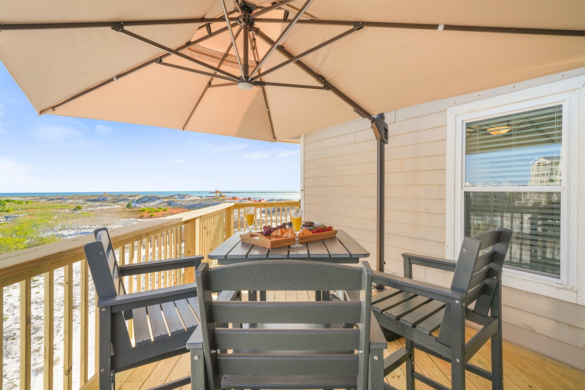 Morning coffee or sunset dinner — the main deck table seats 4 under an umbrella with the dunes and Gulf stretching out below.