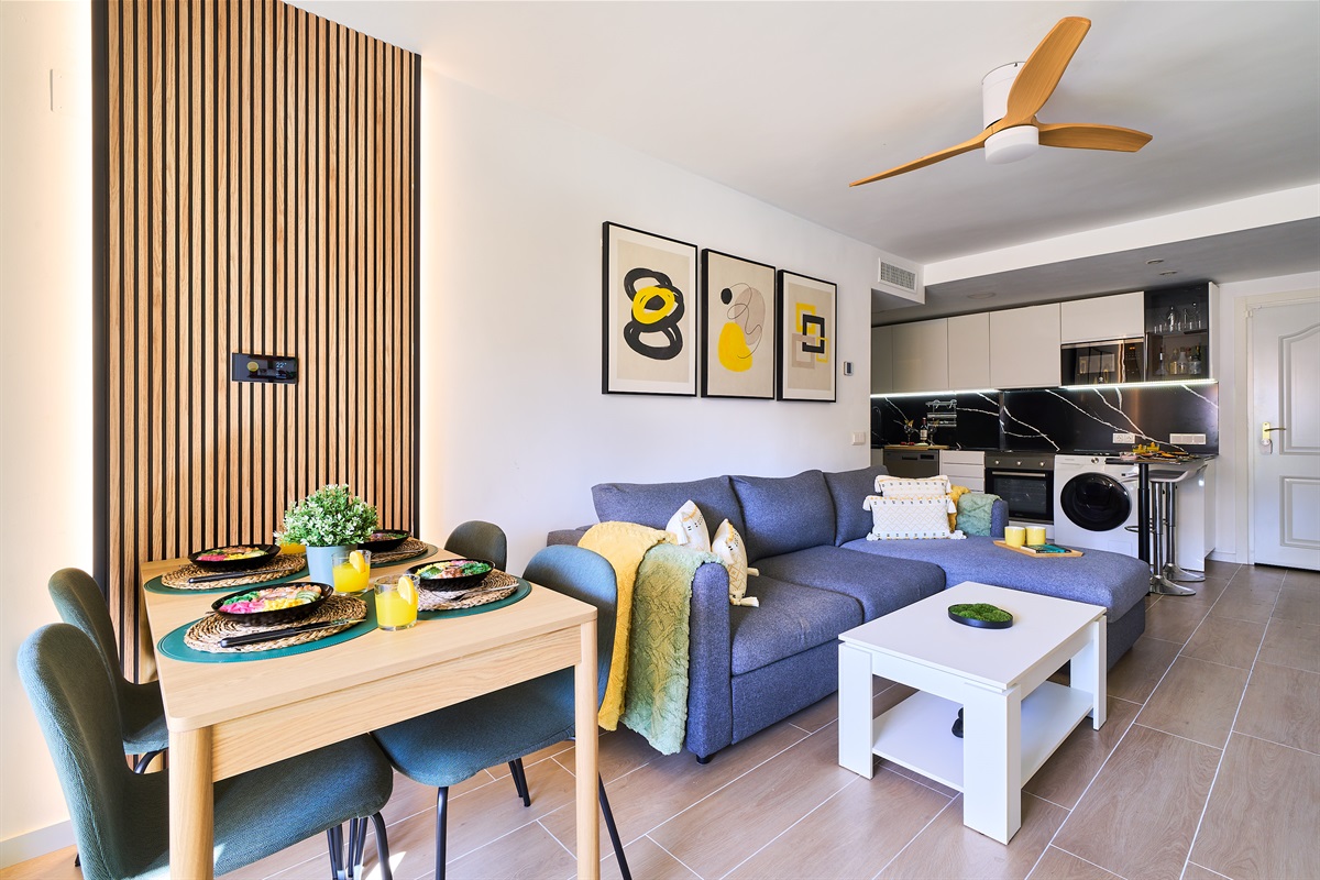 Stylish open-plan living room with a modern kitchen, smart TV, and natural light throughout — ideal for relaxing or sharing a glass of wine after a day by the beach.