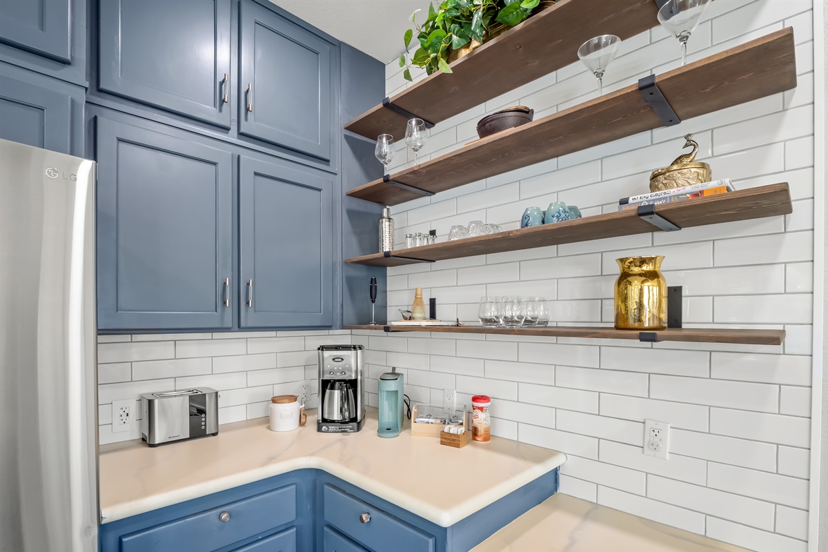 Fully stocked coffee station with drip coffee maker, toaster, electric kettle, mugs, wine glasses, and open shelving for easy access—everything you need for relaxed mornings at home.