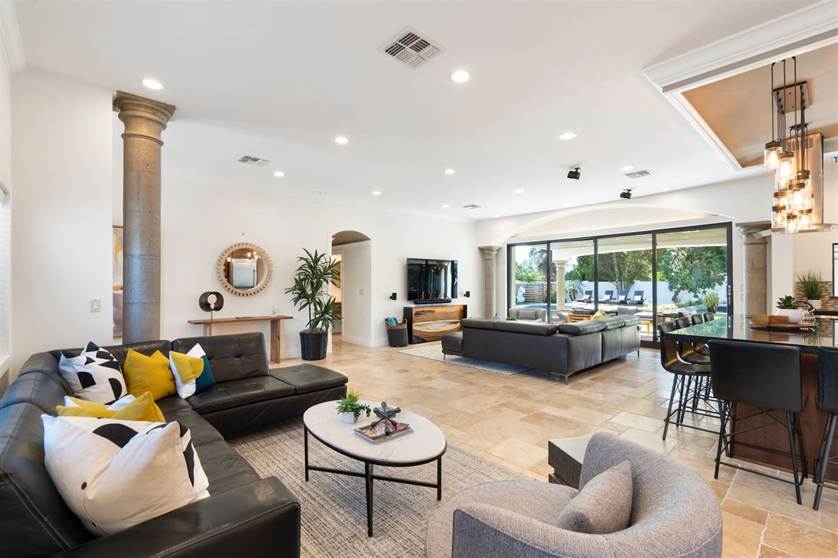Experience luxury living! Our spacious living room features a stunning view of the pool, a sleek black sofa, and a large TV with Sonos speakers for the ultimate entertainment experience. Your perfect escape starts here!