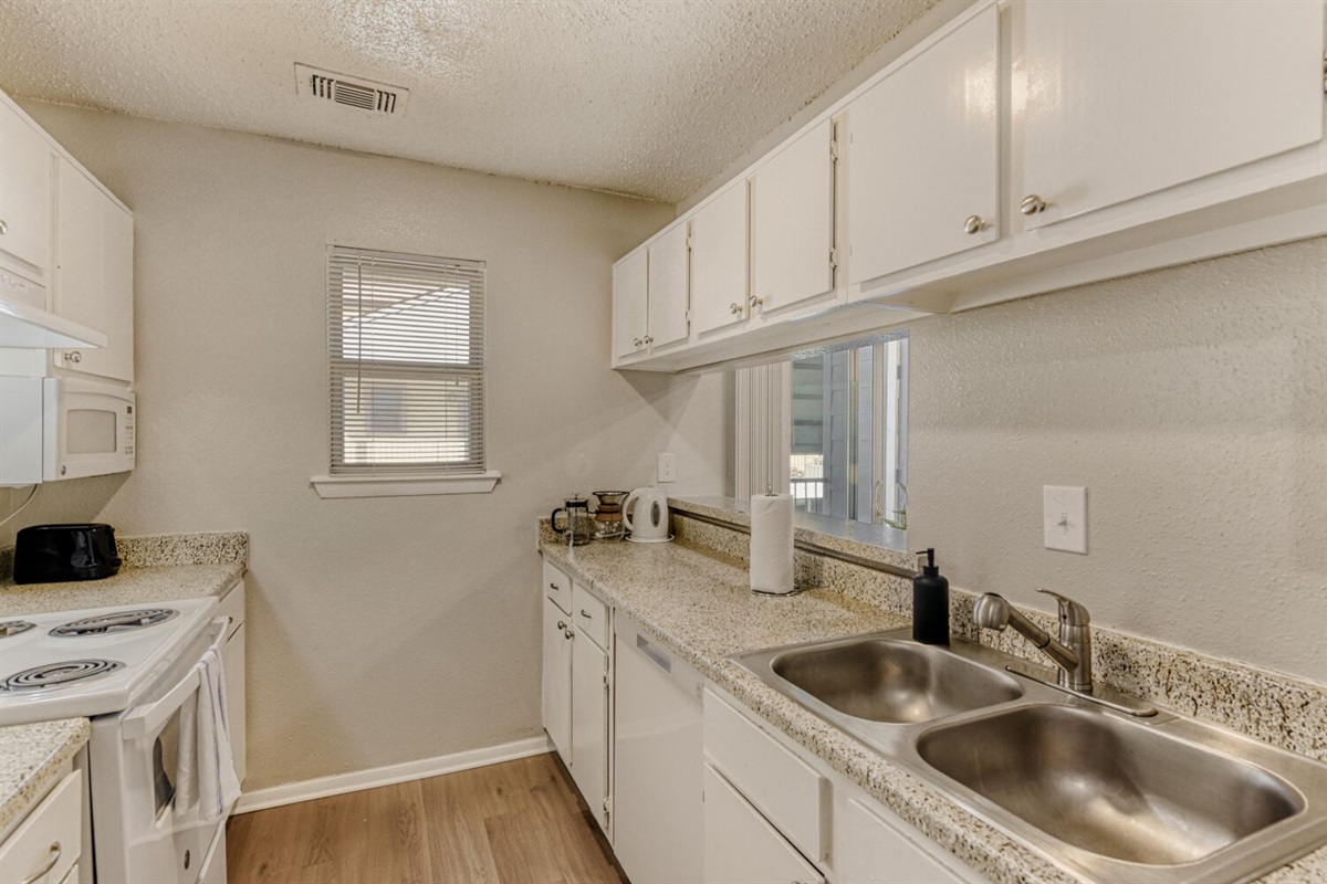 A bright and efficient galley kitchen featuring sleek white cabinetry, granite countertops, and warm wood flooring for a clean, inviting feel.
