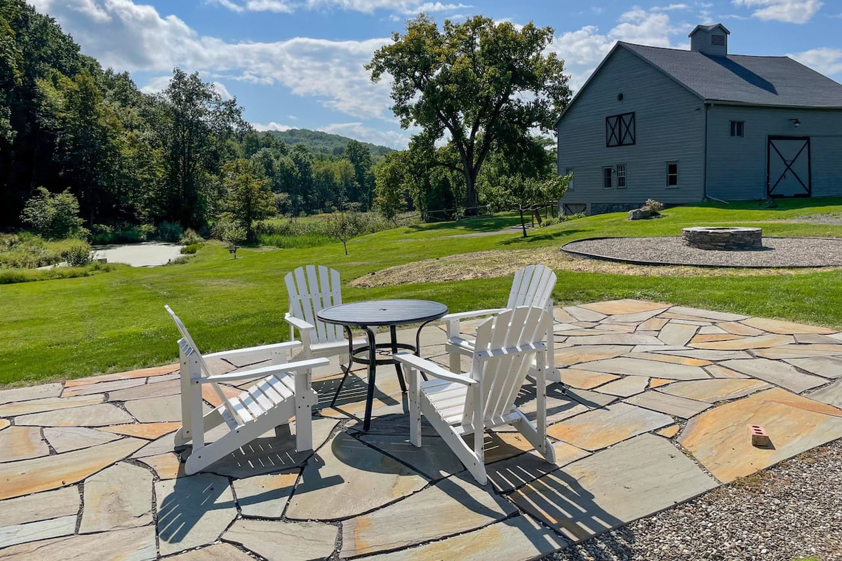The patio and fire pit sit between the house and barn apartment. The fields slope down towards a pond. Private road access continues up the mountain.
