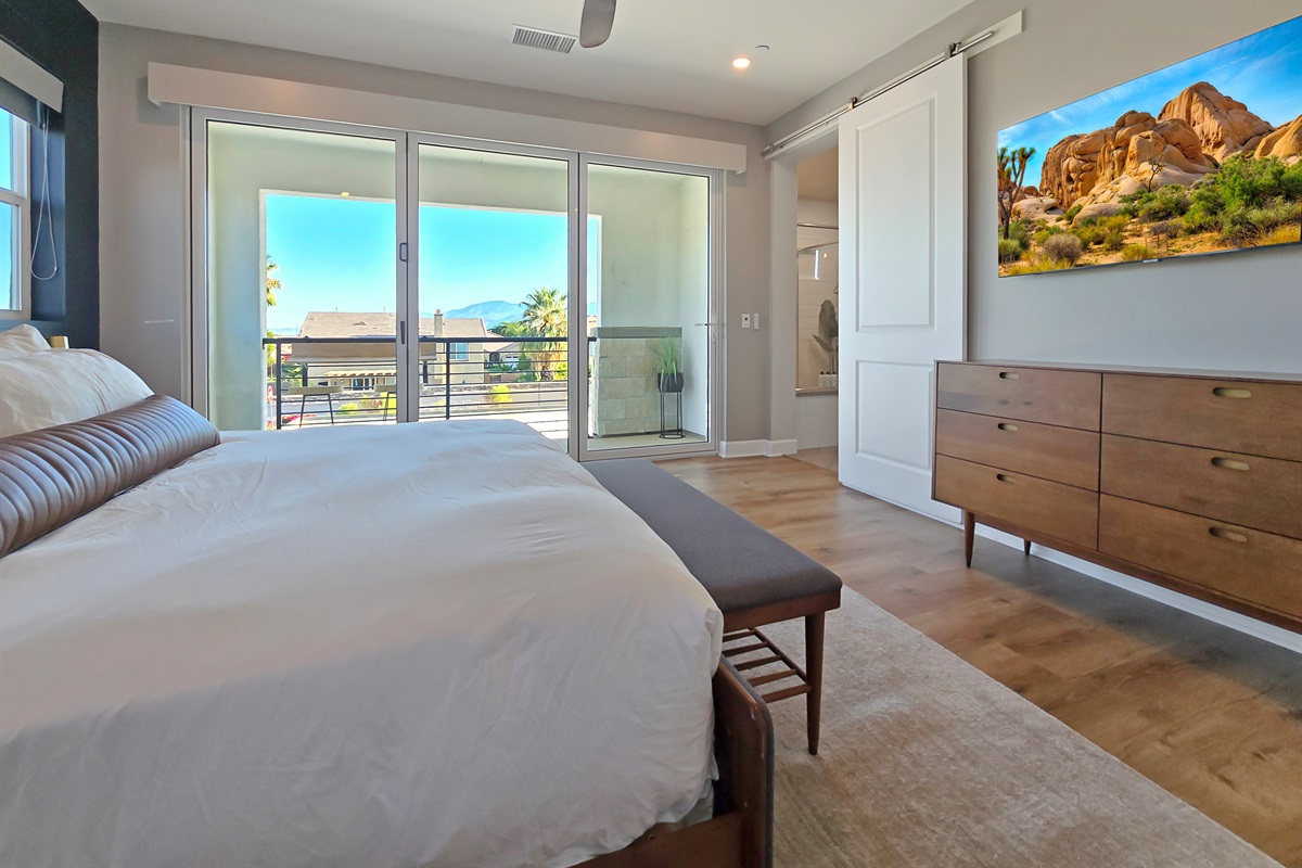 Bedroom #4 upstairs primary suite features a king-sized bed, bi-folding glass doors with a private balcony, ceiling fan and smart TV.