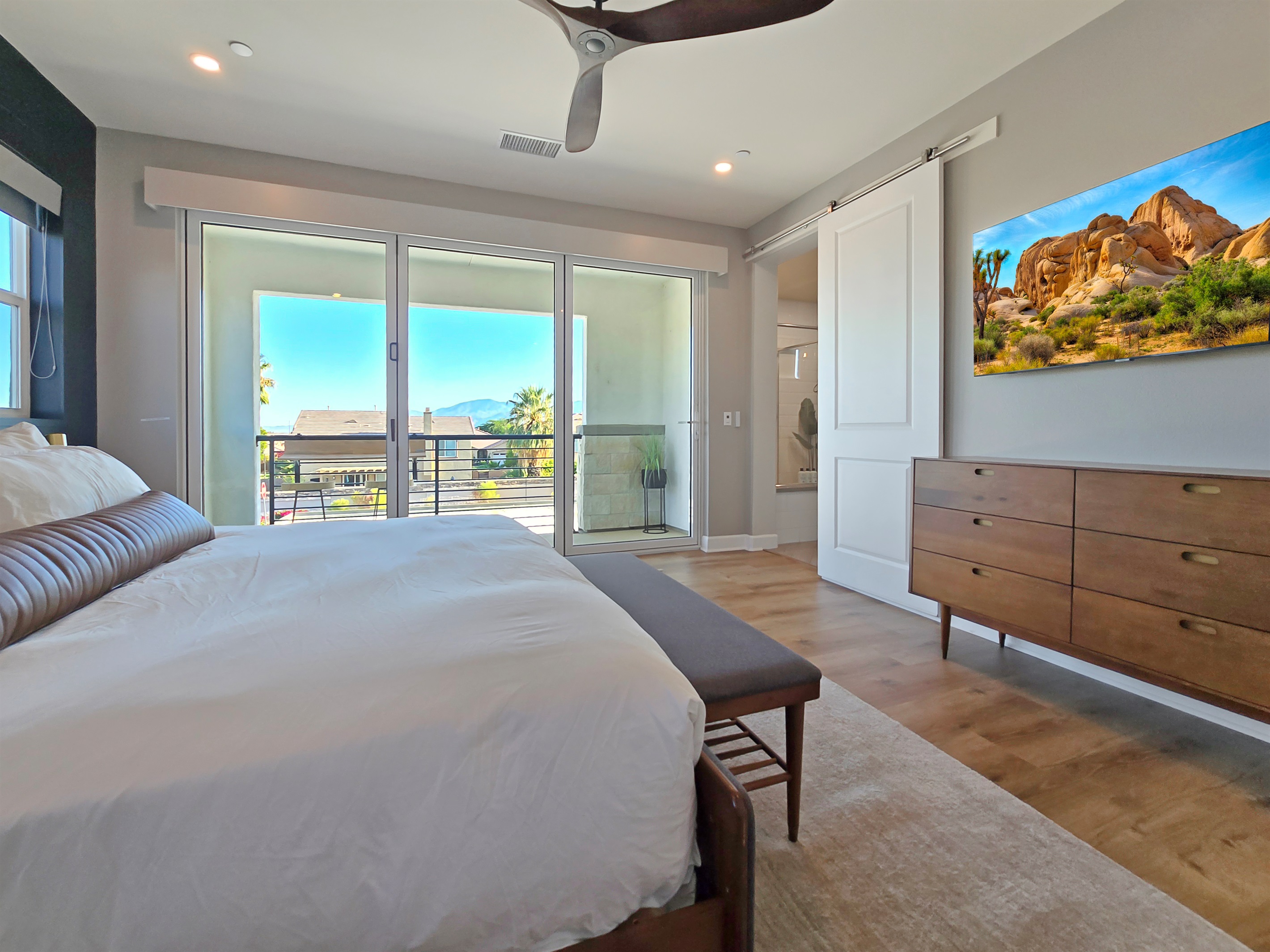 Bedroom #4 upstairs primary suite features a king-sized bed, bi-folding glass doors with a private balcony, ceiling fan and smart TV.