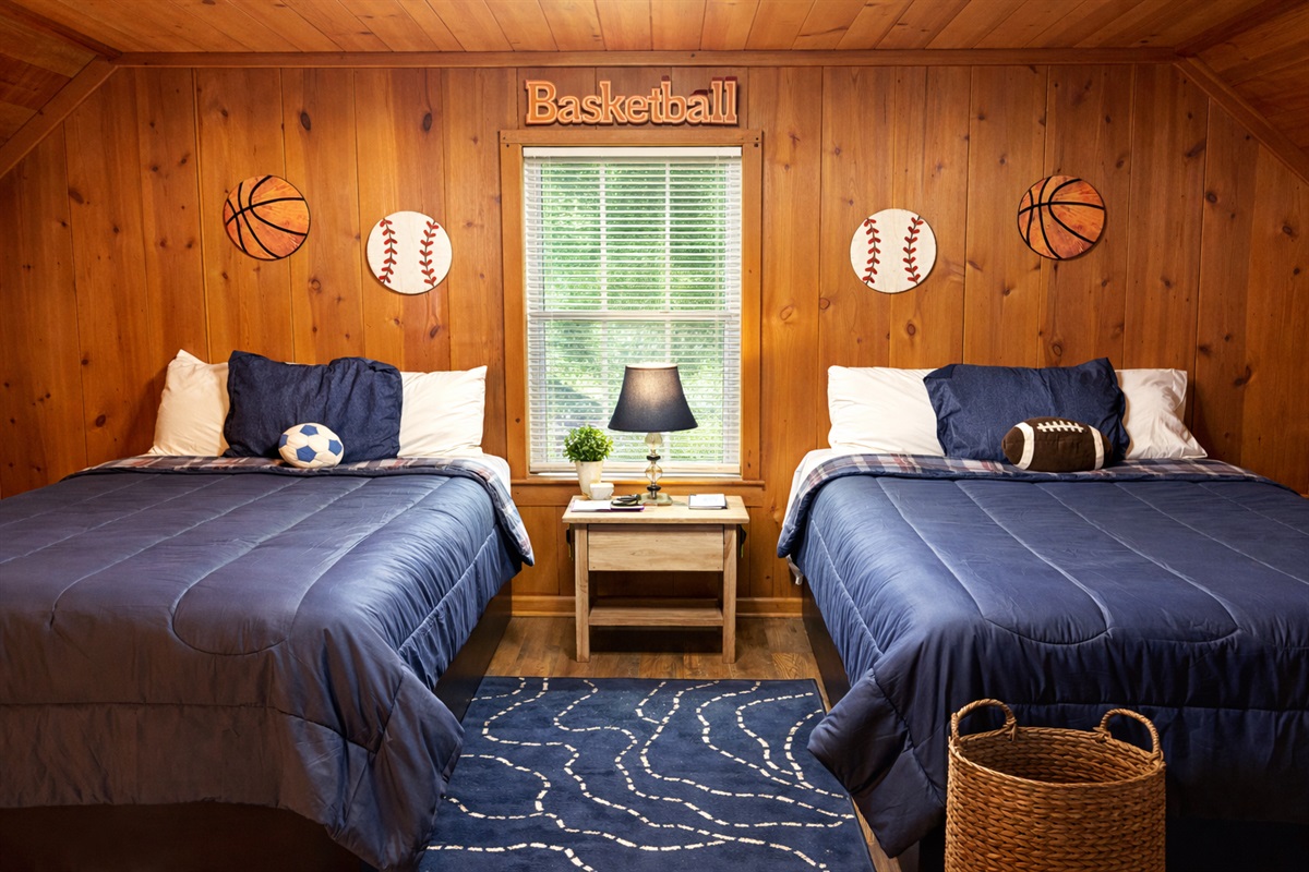 Cozy cabin bedroom with two comfy beds, warm wood walls, and a relaxing reading chair — the perfect place to unwind after a day exploring the mountains.