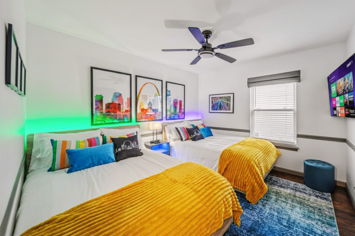 Family-friendly bedroom "The Attractions Suite" featuring two full beds and colorful St. Louis attraction-themed decor.