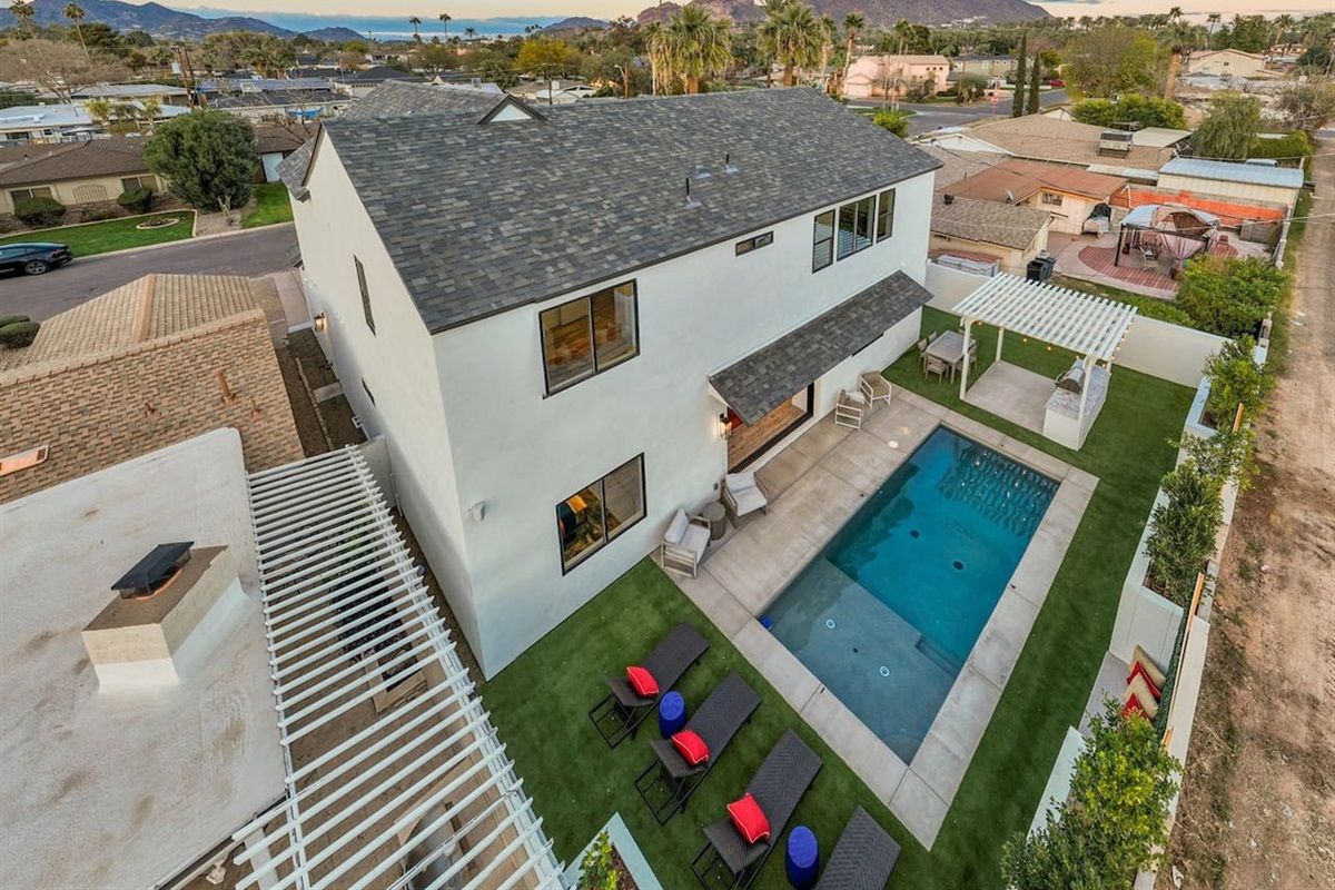 The aerial view of the house captures its luxurious charm, showcasing the private backyard with a crystal-clear heated swimming pool at the center. Surrounding the pool, sun loungers are neatly arranged, perfect for relaxation under the sun.