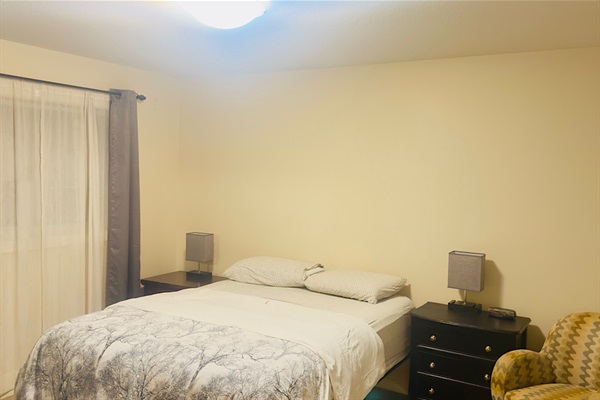 Bedroom with comfy queen sized bed, dual nightstands, walk in closet and accent chair.