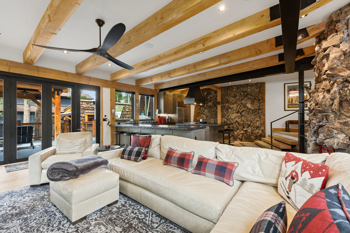 Living room demonstrating open concept with kitchen in background, steps to wet bar on far right and outdoor living space on far left