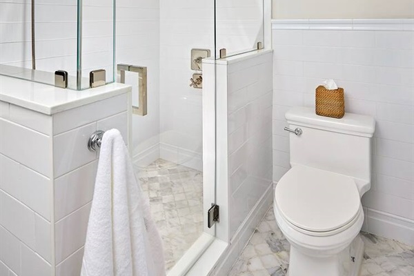 Relax in the stunning ensuite bathroom, featuring elegant Carrara marble floors, a spacious walk-in shower with a sleek frameless glass enclosure, and Kohler polished nickel shower fixtures, including a convenient handheld.