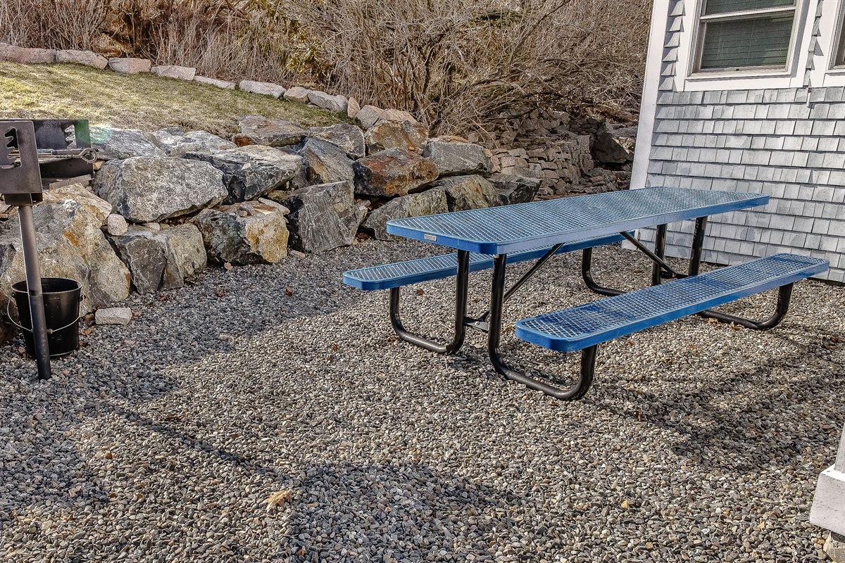 A classic picnic table is ready for your group, nestled against a retaining wall of genuine Maine granite. This dedicated outdoor space, featuring a built-in charcoal grill, provides a relaxed, authentic atmosphere for refuel and recovery after your hike.