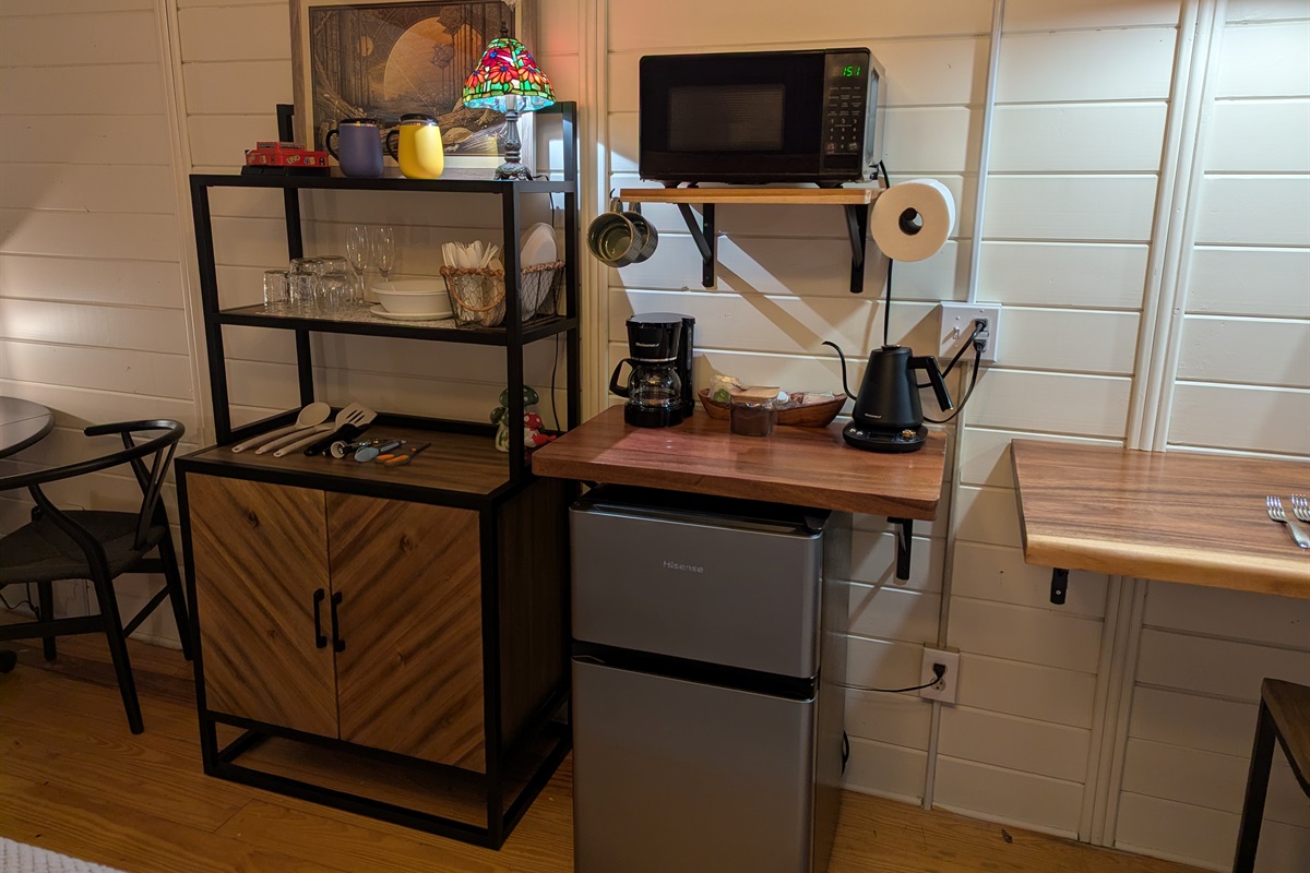Mini Fridge with Freezer, microwave, drip coffee maker, electric kettle, plenty of dishes and drinkware. In cupboard is our electric burner with some pans and skillet. 