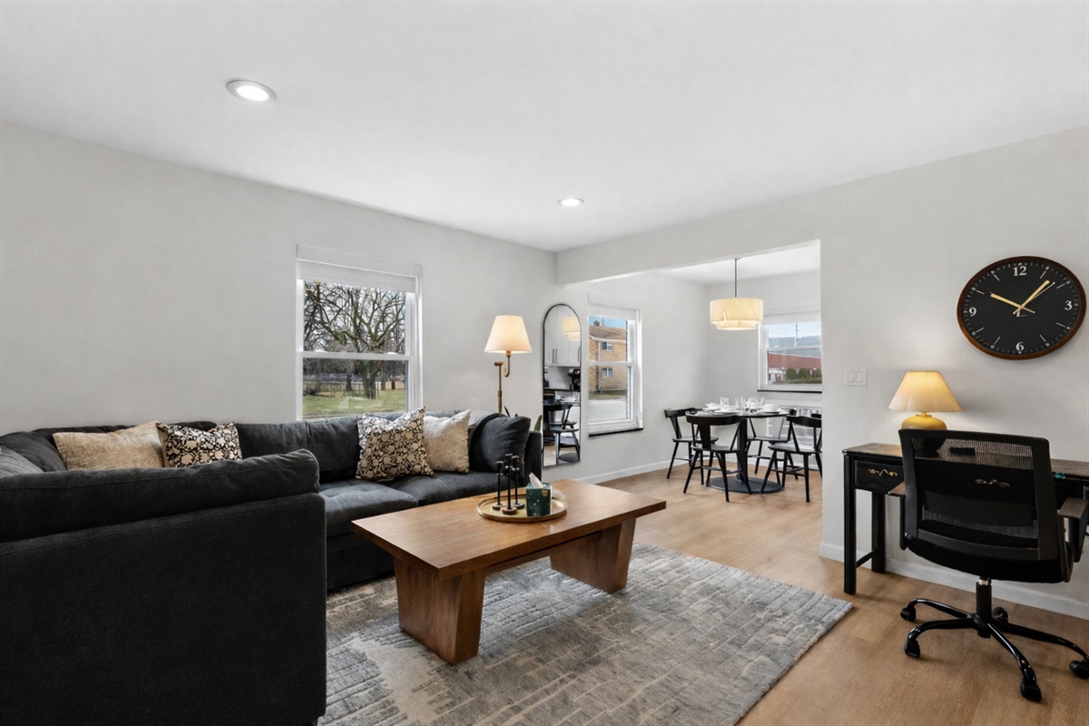 Relax in this bright, open living space with plush sectional seating, stylish décor, and a dedicated workspace flowing into a cozy dining area.