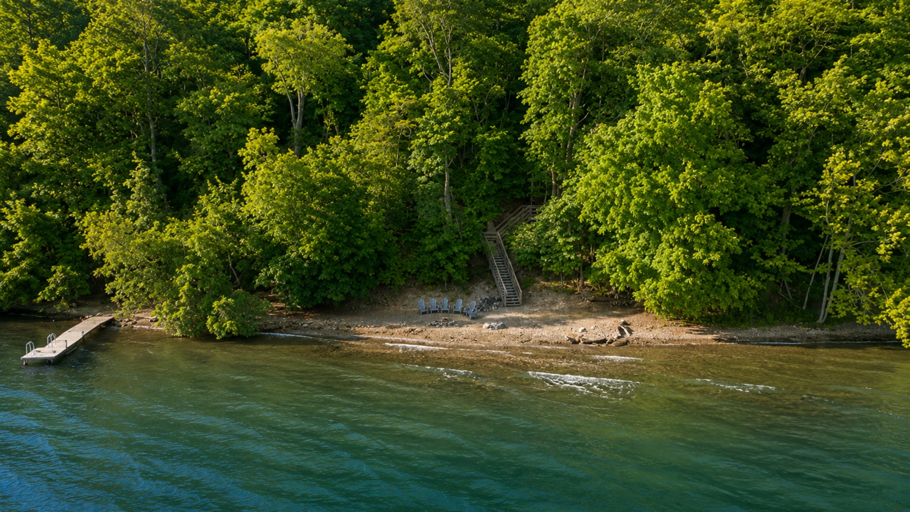 Aerial view of a private, wooded shoreline retreat with direct lake access, dock, and Adirondack chairs for lakeside relaxation.
