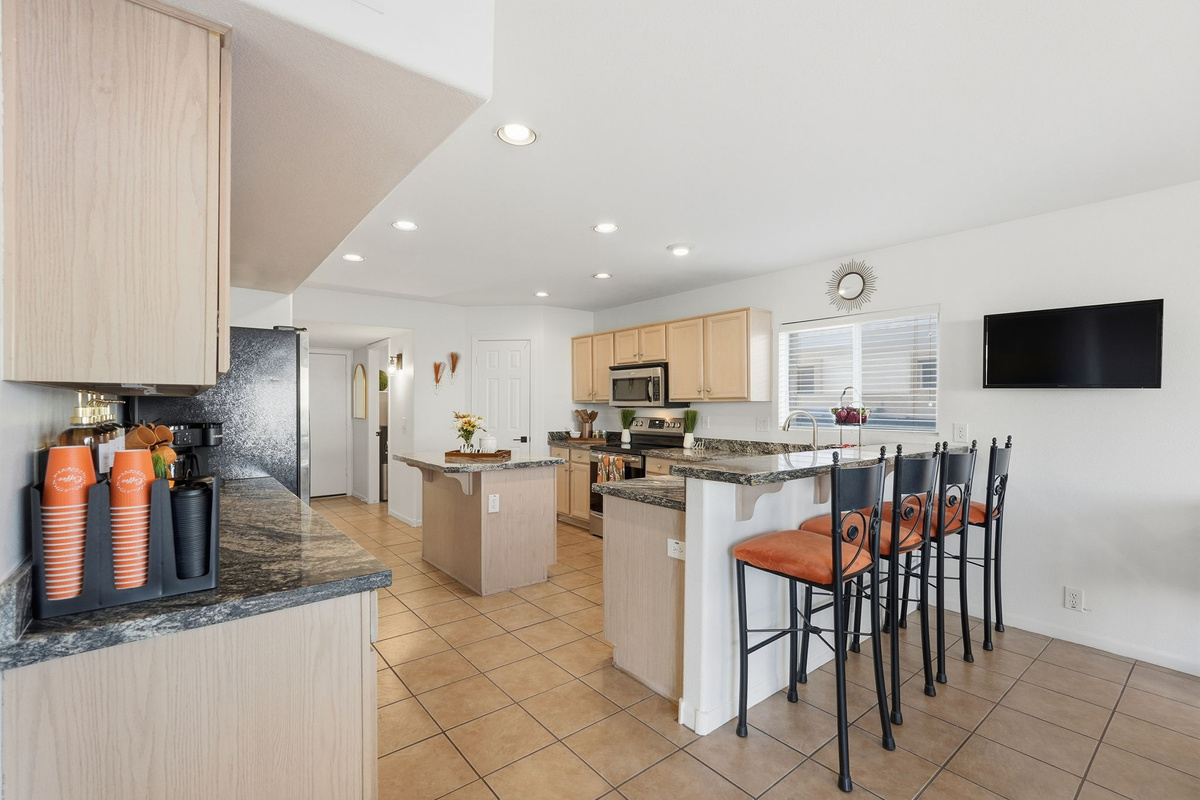 Kitchen breakfast bar with counter seating, granite counters, and open views across the full kitchen and entry area.