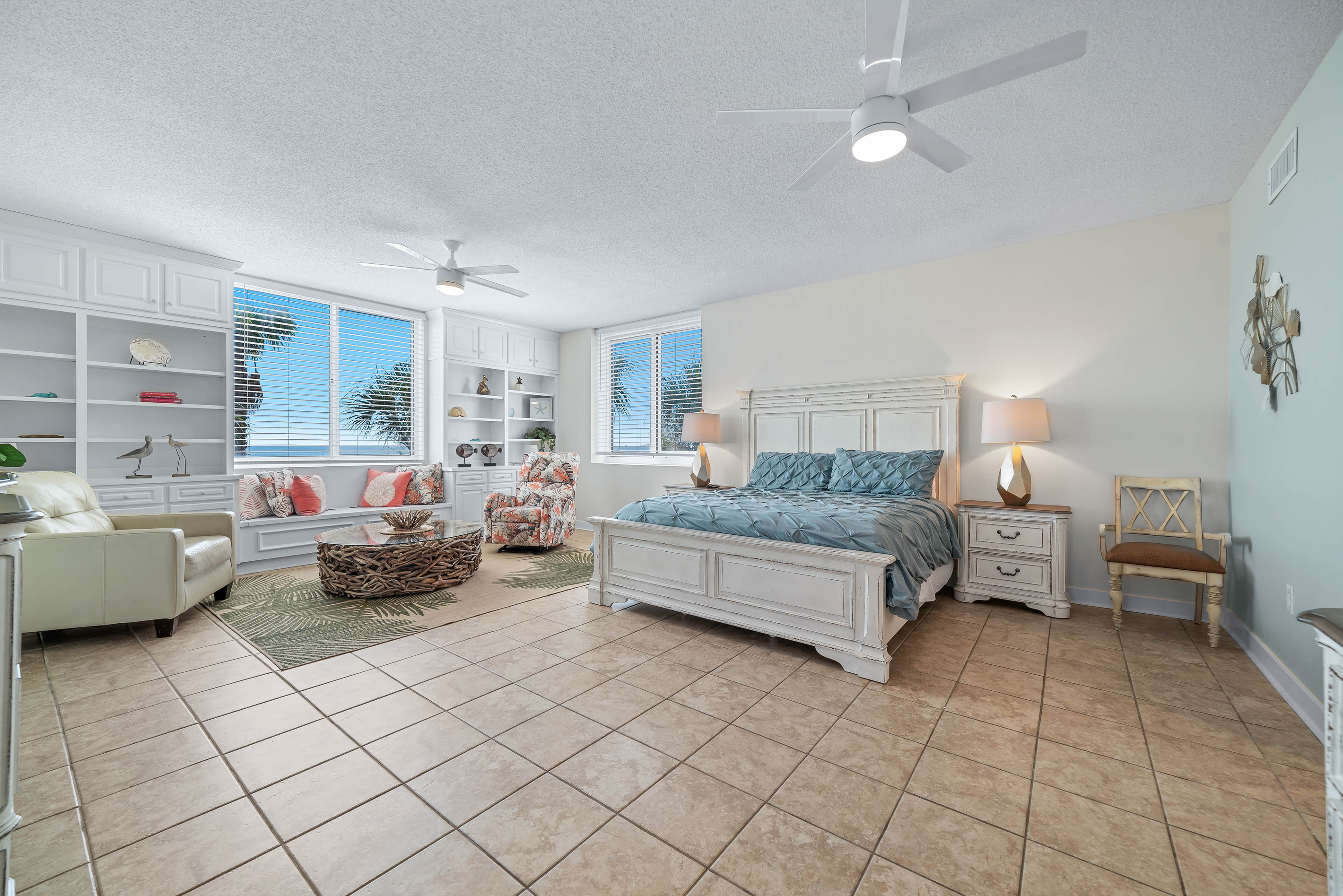 This tranquil primary bedroom is bathed in natural light, showcasing built-in shelving, a comfortable seating area, and stunning views.